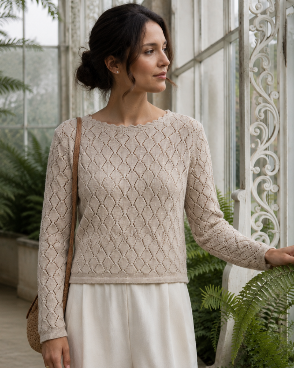 A woman stands in a greenhouse wearing a beige textured knit long-sleeve top and white wide-leg trousers, with a brown shoulder bag.